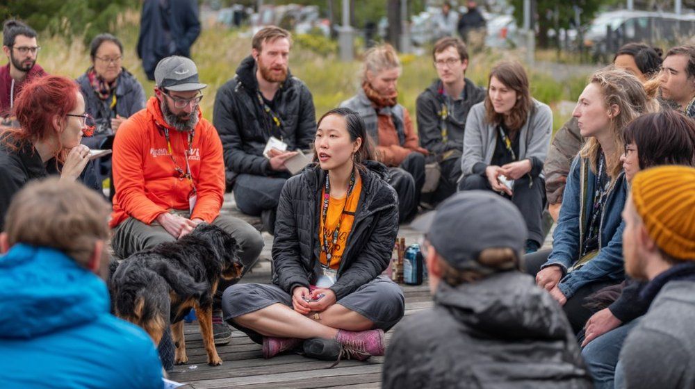 A community organizer speaking to a diverse group in an outdoor circle meeting