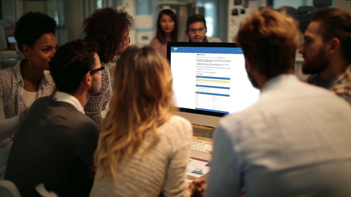 A diverse civil rights advocacy team gathered around a monitor reviewing their ALIS intake dashboard